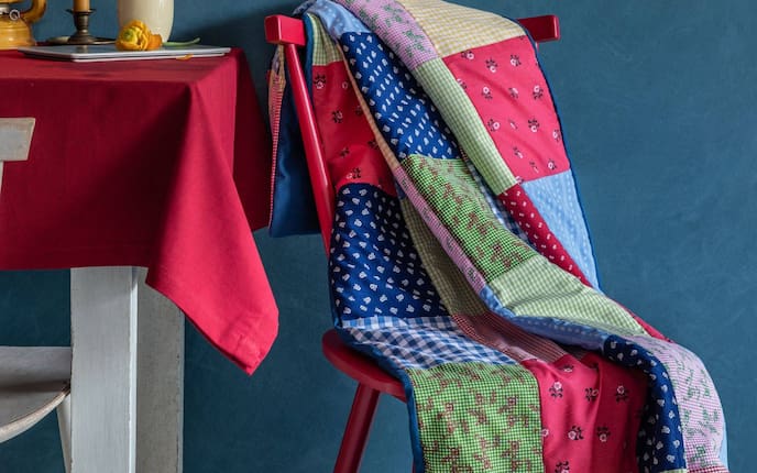 Bunte Flickendecke aus Dirndlstoff, roter Holzesessel, weißer Holztisch mti roter Tischdecke