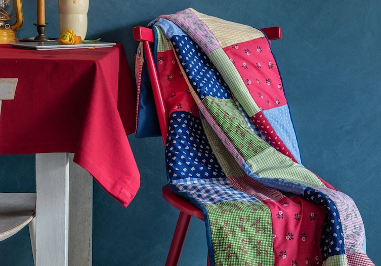 Bunte Flickendecke aus Dirndlstoff, roter Holzesessel, weißer Holztisch mti roter Tischdecke