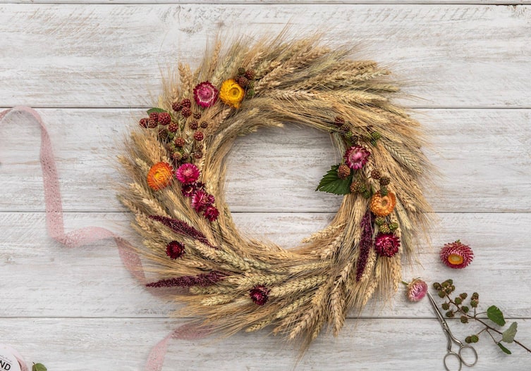 Ährenkranz mit Stroblumen und Brombeeren liegt auf einem weißen Holzuntergrund