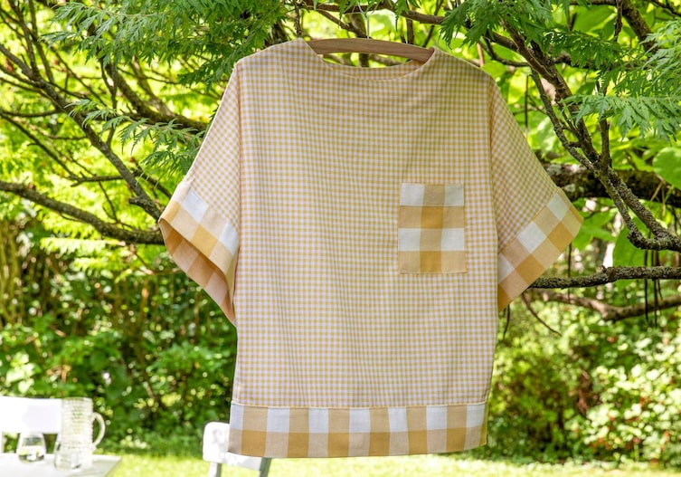 Gelb karierte Blus mit kurzen Ärmeln hängt auf einem Kleiderbügel in einem Baum