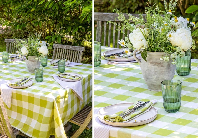 Verwitterte Holzsessel stehen rund um einen Gartentisch, der mit einem grün-karierten Tischtuch, grünen Gläsern, Tellern , Besteck und grünkarierten Stoffservietten gedeckt ist. Am Tisch steht noch alter Tonkrug mit weißen Pfingstrosen, Margariten und Wienseblumen.