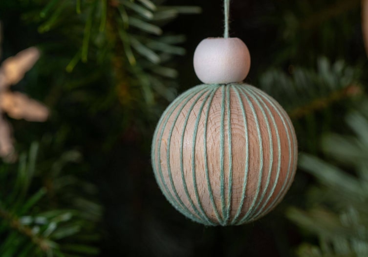 Holzkugel mit Stickgarn eingewickelt, hängt auf einem Christbaum.