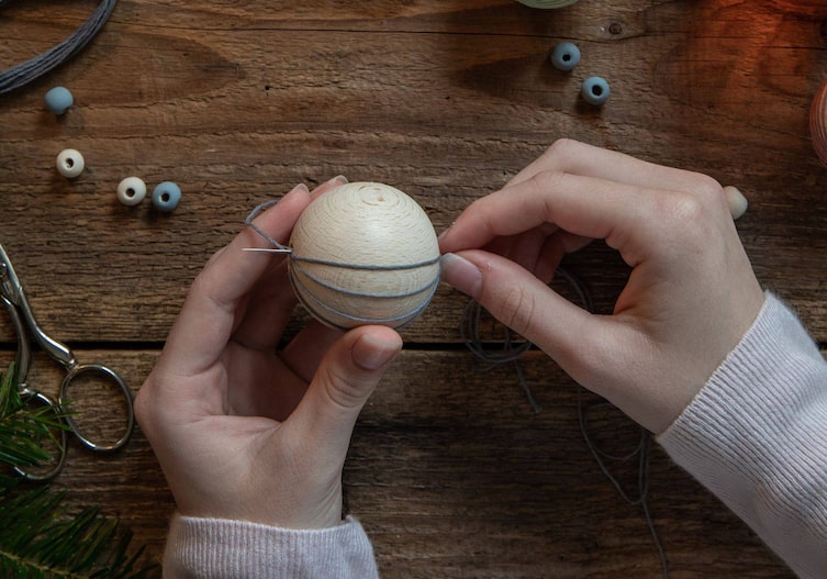 Holzkugel wird mit einer langen Nadel und dem Stickgarn umwickelt.