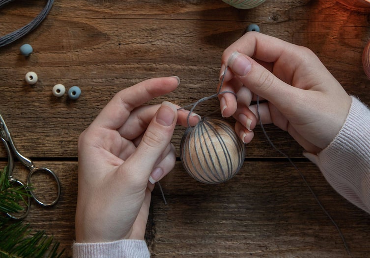 Zwei Frauenhände verknoten die beiden Enden des Garns, das um die Christbaumkugel gewickelt wurde.