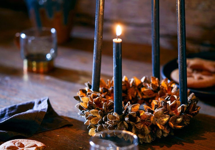 Bucheckernkranz vergoldet mit dunklen Stabkerzen, alles steht auf einem dunklen Holztisch.