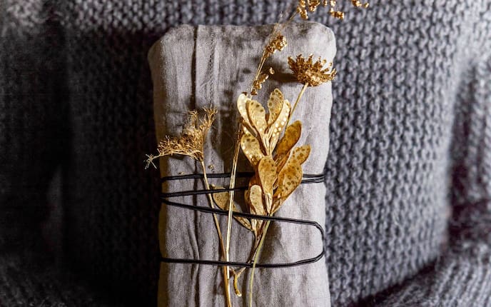 Geschenk in ein graues Tuch gewickelt und mit in Gold getauchten Herbstgräsern geschmückt.