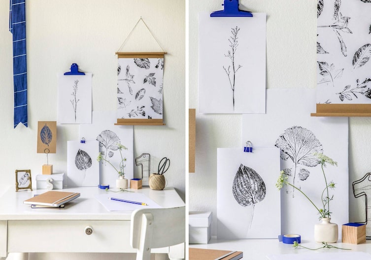 Eine weiße Wand, ein weißer kleiner alter Holztisch, davor steht ein weißer alter Sessel. And der Wand hängen Linoldrucke von Blättern auf weißem Papier gedruckt. Als zusätzliche Farbe wird blau bei der Dekoration verwendet (Stoffband, Wandhalterung für den Druck).