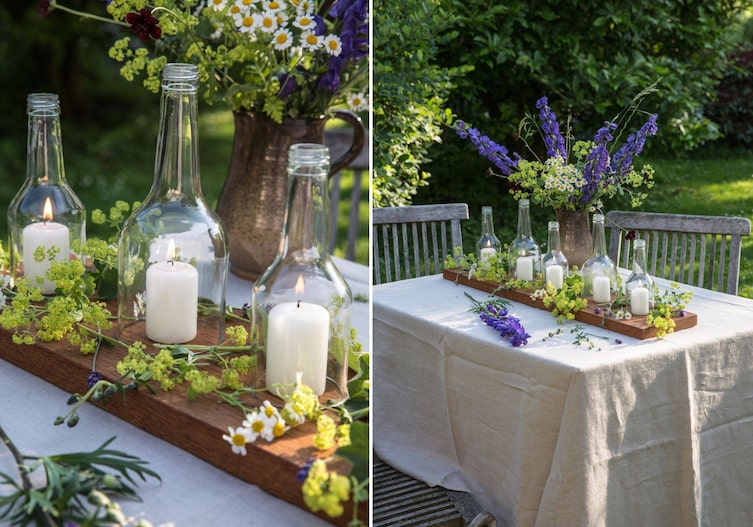 Sommer, Garten, Gartentisch mit Tischtuch, darauf steht ein Sommerlicher Blumenstrauß und ein Holzbrett mit Windlichtern aus Flaschen und Kerzen und Sommerblumen dekoriert