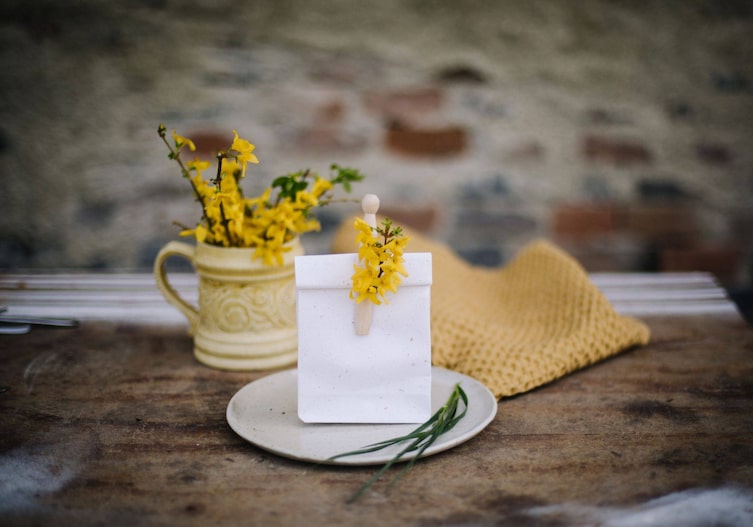 Holztisch auf dem ein Teller steht, darauf ist ein Papiersackerl mit einer Holzkluppe, mit der ein kleiner Forsythienzweig befestigt ist