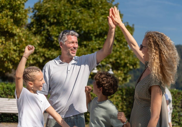 Familie mit zwei Kindern und zwei Erwachsenen beim High-Five in einem sonnigen Park in der Donauregion Oberösterreich
