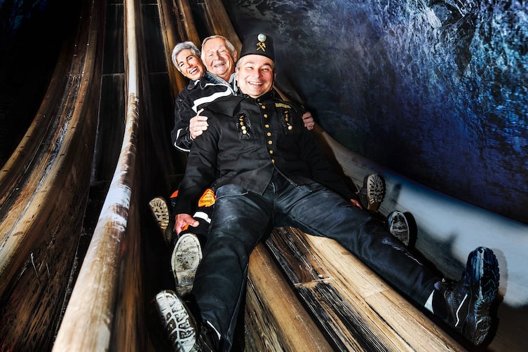 Drei Personen rutschen eine Rutsche im Salzbergwerk Berchtesgaden hinunter.