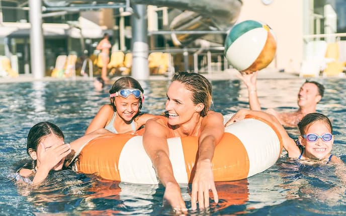 Zu sehen ist eine Familie mit Schwimmreifen und Wasserbal in einem Pool.