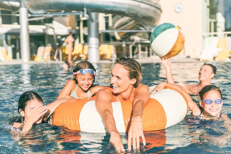Zu sehen ist eine Familie mit Schwimmreifen und Wasserbal in einem Pool.