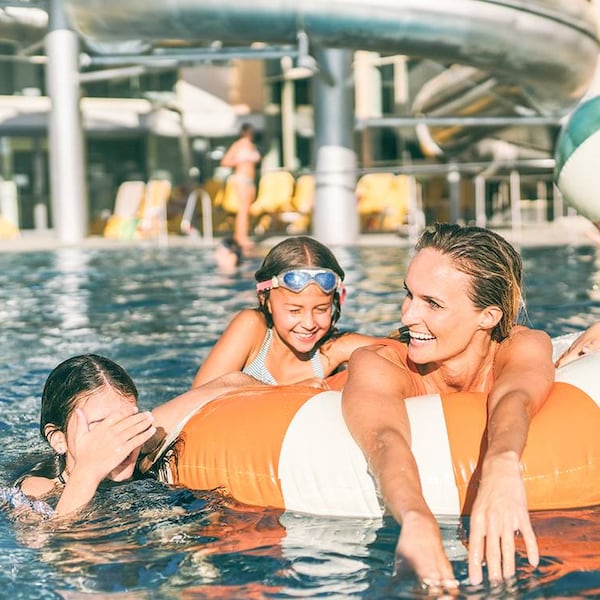 Zu sehen ist eine Familie mit Schwimmreifen und Wasserbal in einem Pool.
