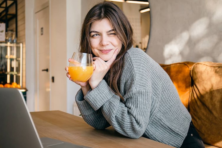 eine junge frau sitzt am tisch und trinkt ein glas orangensaft
