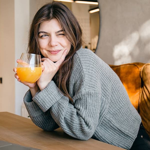 eine junge frau sitzt am tisch und trinkt ein glas orangensaft