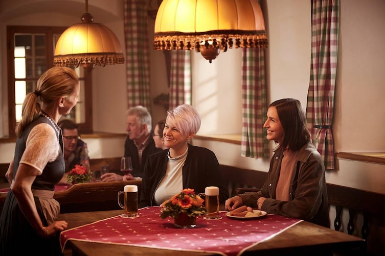 Zwei Frauen sitzen im Wirtshaus und plaudern mit der Kellnerin.