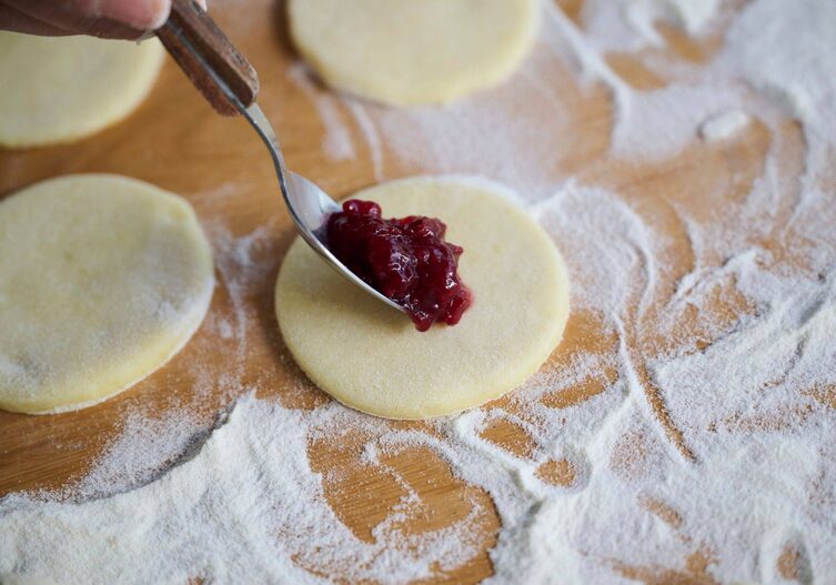 Mit einem Löffel wird rote Marmelade auf einen ausgestochenen Kreis aus Erdäpfelteig gegeben.