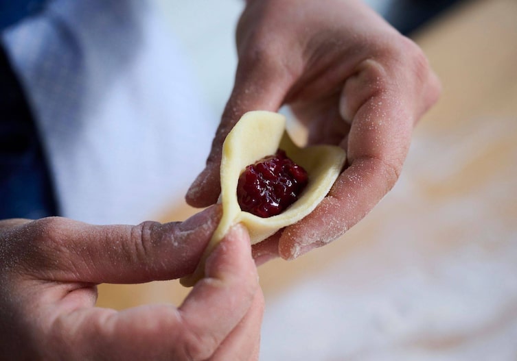Hände formen aus Erdäpfelteig und roter Marmelade ein süßes Tascherl.