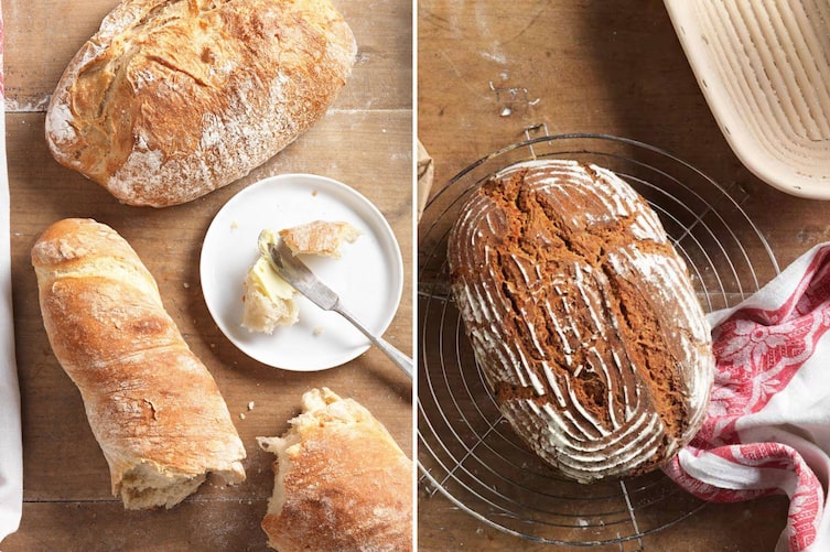 Draufsicht auf ein bemehltes Holzbrett mit einem runden, goldbraun gebackenen Weizenlaib und einem aufgebrochenen Baguette. Auf einem kleinen weißen Teller liegt ein Buttermesser mit etwas Butter, links ein weißes Küchentuch. Daneben: Rundlaib mit dunkler, rilliger Kruste auf einem runden Drahtgitter-Abkühlrost auf einem Holztisch. Das Muster stammt von einem Gärkorb, der im Hintergrund zu sehen ist. Ein rot-weißes Küchentuch ist um den Laib gelegt.