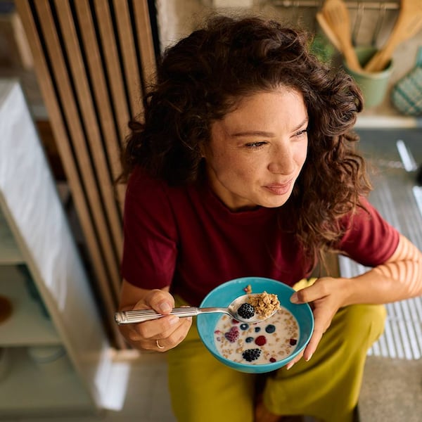 Eine Person isst ein gesundes Frühstück mit Müsli, Beeren und Milch in einer modernen Küche.