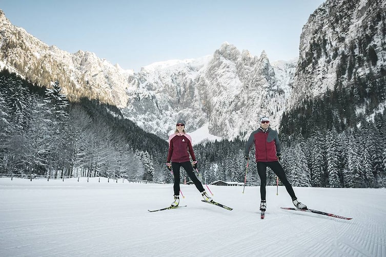 Zwei Langläufer im Nationalpark Berchtesgaden auf gespurter Loipe mit schneebedeckten Bergen im Hintergrund.