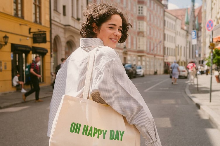 Zu sehen ist eine Frau, die einen weißen Stoffbeutel mit der Aufschrift "Oh Happy Day" trägt.