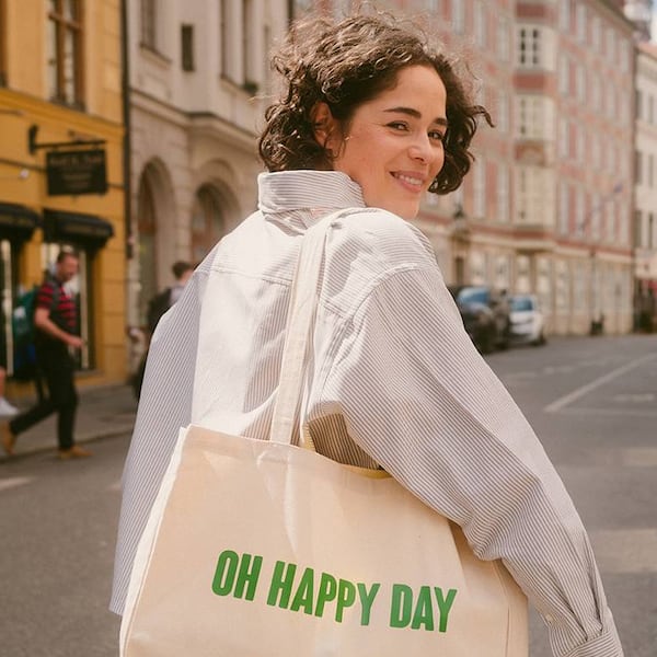 Zu sehen ist eine Frau, die einen weißen Stoffbeutel mit der Aufschrift "Oh Happy Day" trägt.