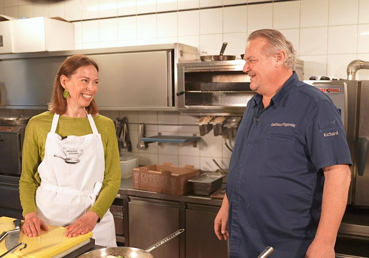 Doris Ahornegger mit Koch Richard Poppmeier in seiner Küche beim Herd.