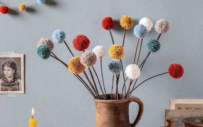 bunter Bommelblumenstrauß, Kerze, Tonkrug, hellblaue Wand