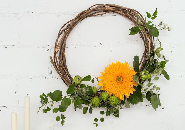 Kranz aus Ästen mit frischen Kastanien und einer gefüllten Sonnenblume.