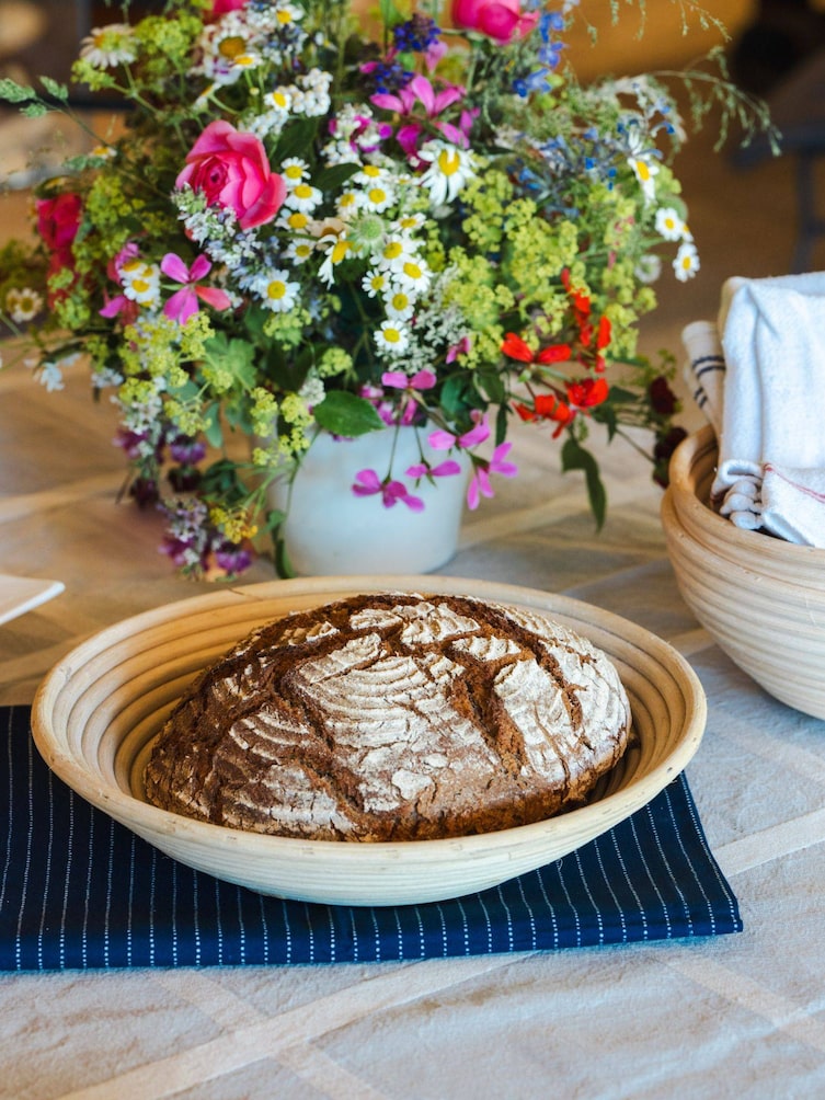 Brot in einem Brotkorb vor einem bunten Blumenstrauß.