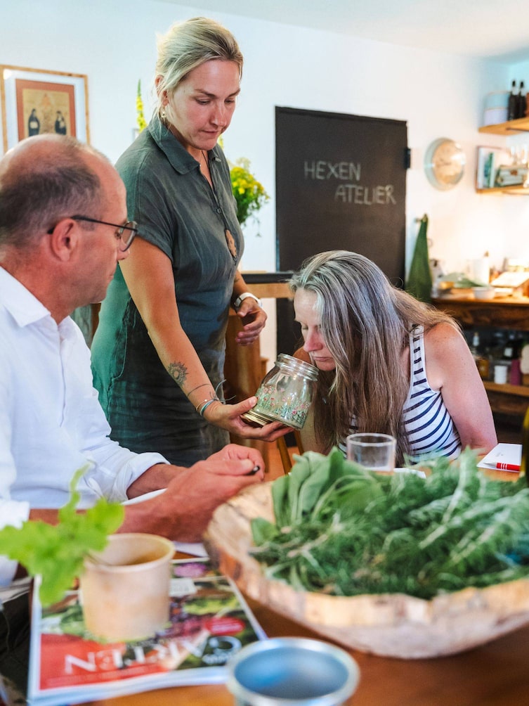 Kräuterexpertin Tanja Mittendorfer hält der Teilnehmerin ein Glas mit pulverisierten Kräutern hin.