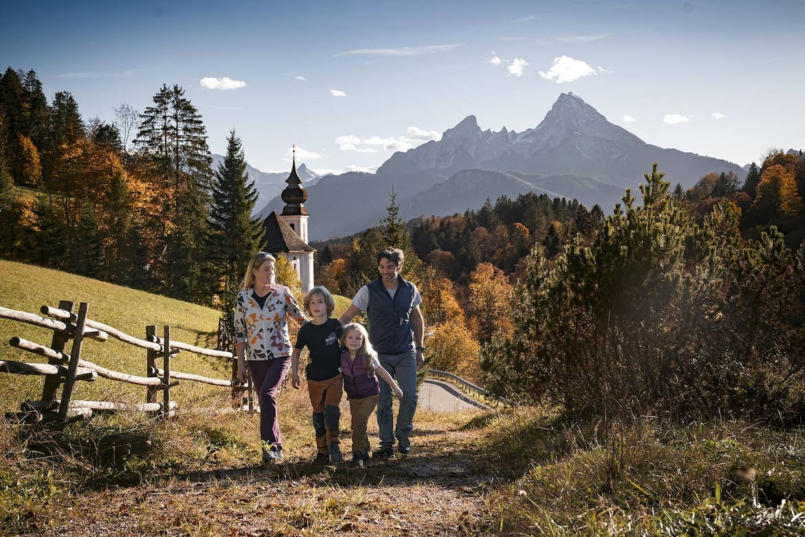 Eine Familie geht einen Waldweg in Berchtesgaden hinauf. Im Hintergrund ist eine Kirche zu sehen.