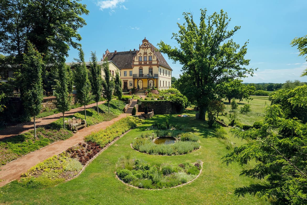 Ein Bild von einem Rittergut umrundet von grünen Bäumen und viel Natur.