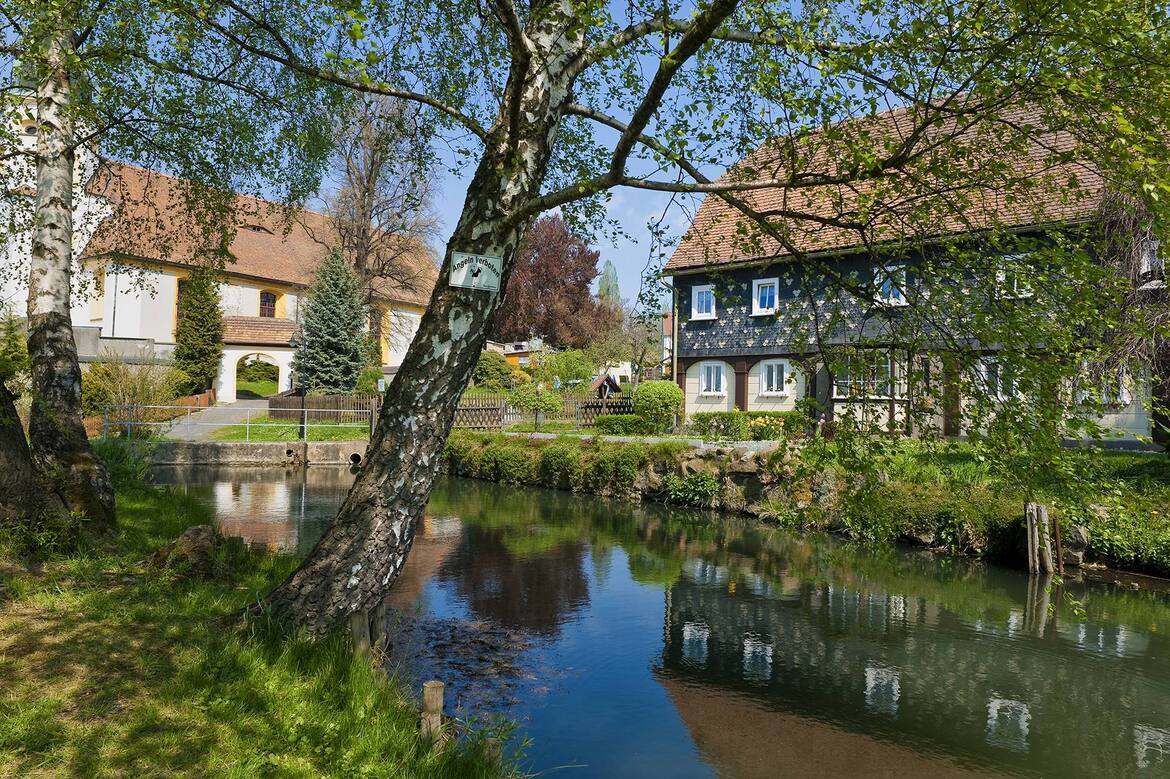 Ein Bach, ein altes Haus und Bäume am Tag.