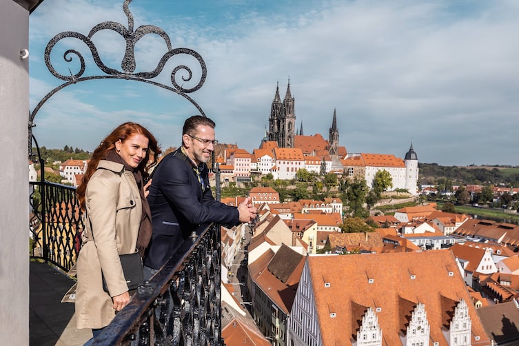 Eine Frau und ein Mann stehen vor einem Geländer und blicken über die Dächer von Meißen.