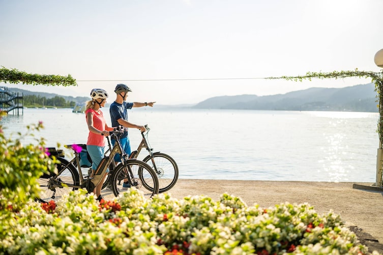 Eine Radfahrerin und ein Radfahrer genießen den Ausblick auf den Kärtner Wörthersee.