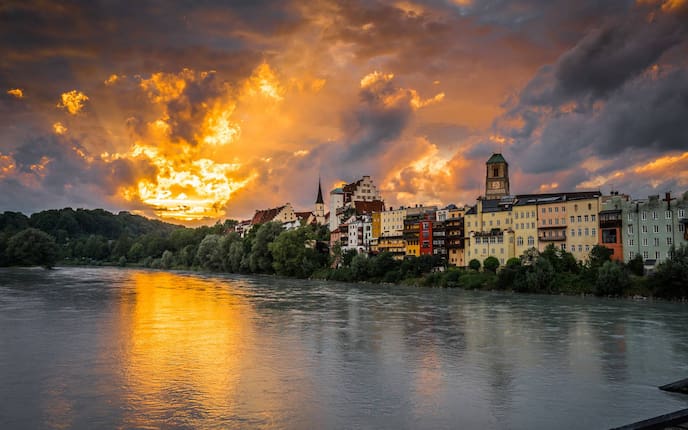 Untergehende Sonne spiegelt sich am Inn vor den historischen Bauten in Wasserburg