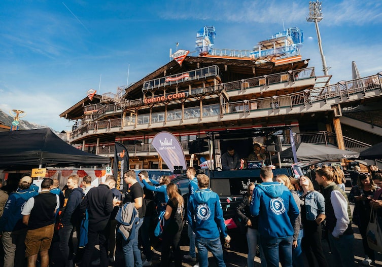 Eine Außenaufnahme von der Tenne Schladming mit vielen Menschen am Parkplatz.
