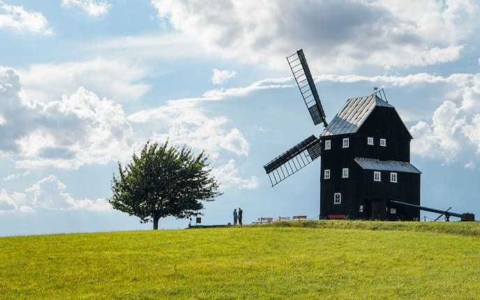 Ein Mühlhaus neben einem Baum mit 2 personen.