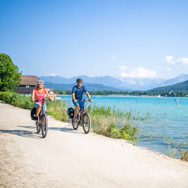 Eine Frau und ein Mann fahren mit dem Fahrrad entlang des Faaker Sees.