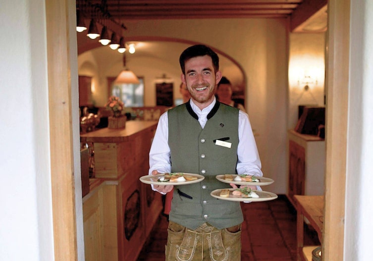 Ein Kellner trägt drei Teller mit Vorspeisen durch eine Tür.