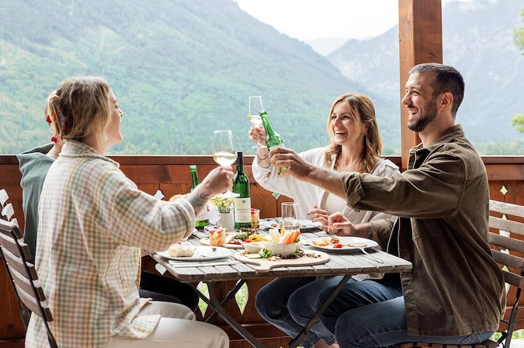 Drei Freunde bei einer gemeinsamen Jause auf einem Balkon mit Blick in die Berglandschaft.