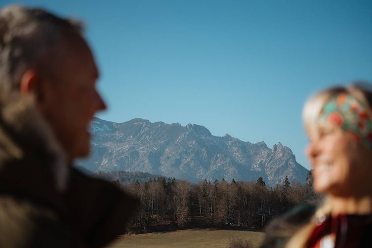 Unscharfer Vordergrund mit Paar, im Fokus das Watzmann-Massiv bei klarer Herbstsicht in Berchtesgaden.