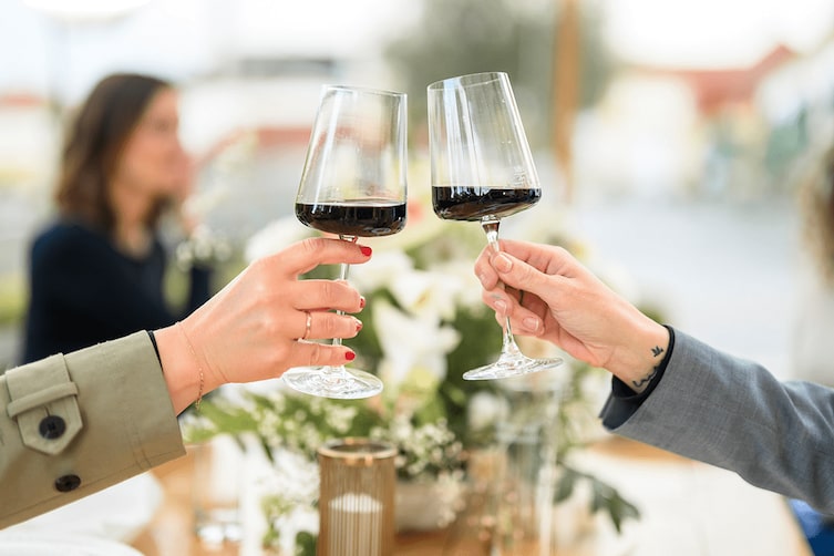 Zwei Weingläser mit Rotwein drinnen, Eine Frau und ein Mann stoßen an im Restaurant.
