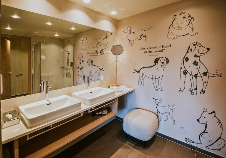 Badezimmer im Hotel DIE WASNERIN mit Doppelwaschbecken, einer riesen Spiegelwand und unterschiedlichen Hunderassen, die an die Wand gemalt sind.