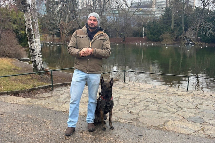 Hundetrainer Florian Günther steht mit seiner Hündin Trude an einem Teich im Wiener Stadtpark. Die beiden sind während der Aufnahme des Hunde-Podcasts auf einem Spaziergang unterwegs.