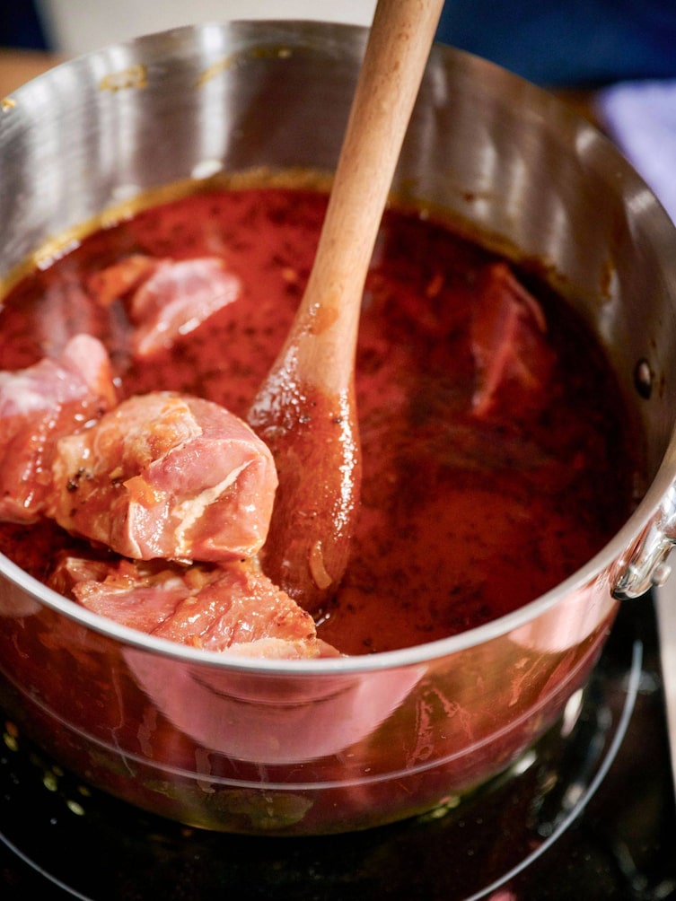 Fleisch in einer roten Sauce, das zu Gulasch wird.