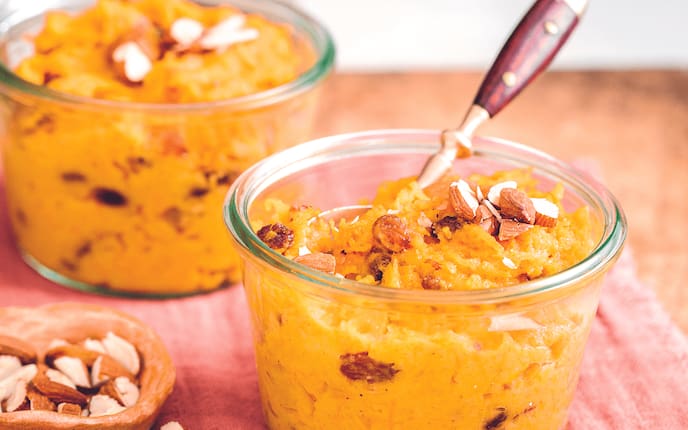 Karotten, Rosinen und gehackten Mandeln in einem Glasschüsserl serviert in dem ein kleiner Teelöffel mit Holzgriff steckt.